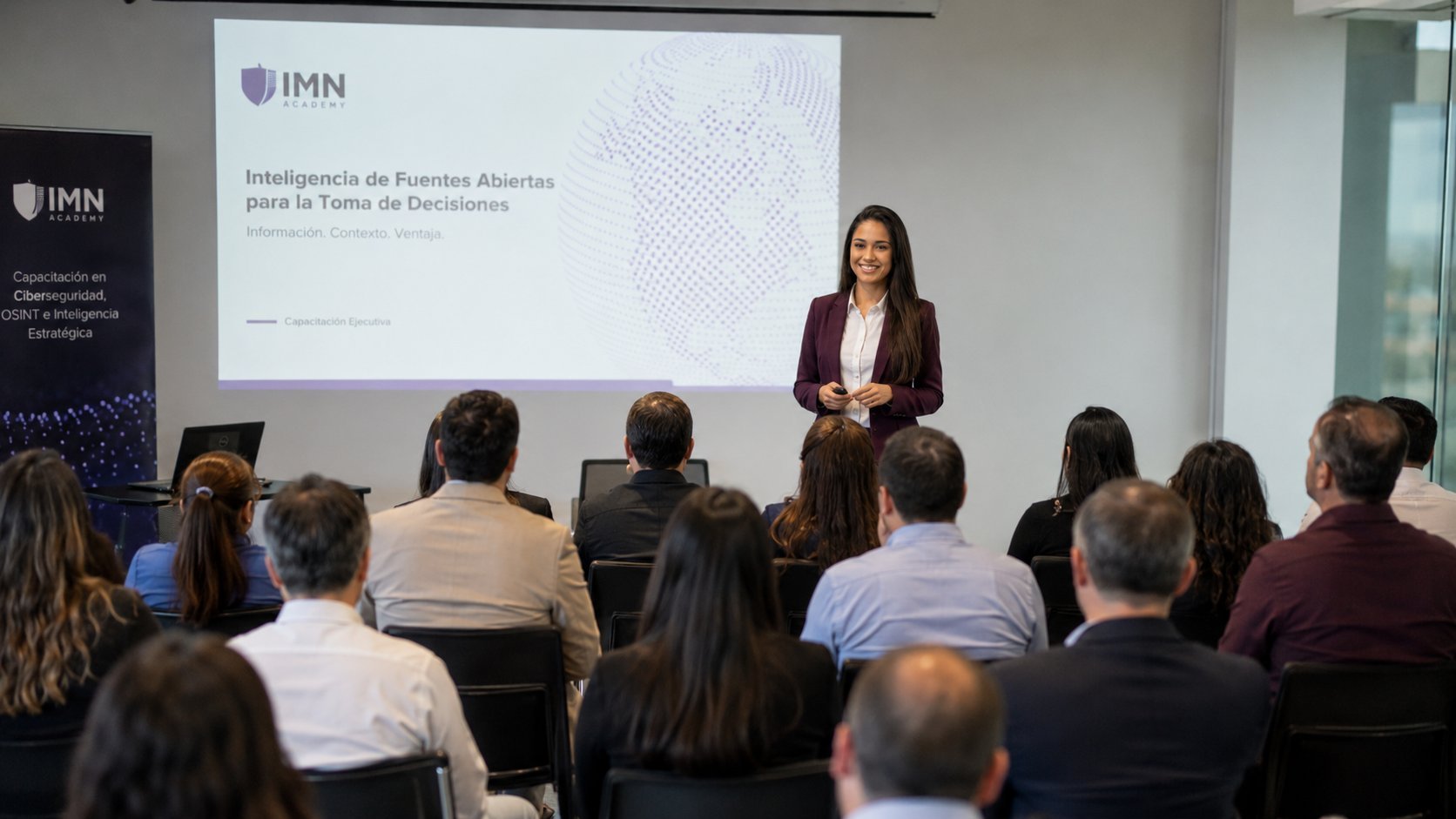 Professional woman presenting on stage to an audience in a conference room with IMN branding and projection screen visible.